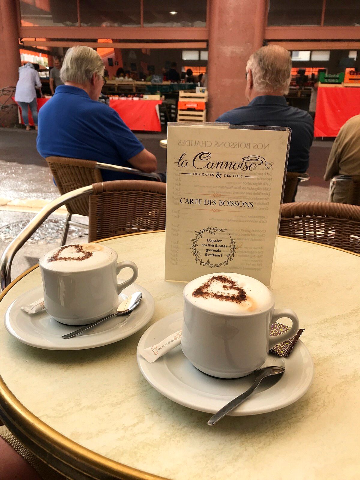 Deux cappuccinos au cœur de cacao sur un guéridon de la terrasse, face au marché Forville